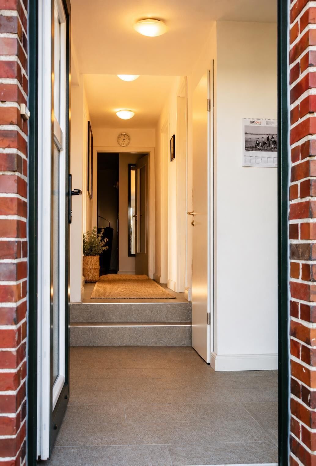 A hallway with a carpeted staircase leading to a door, a clock on the wall, and a framed picture.