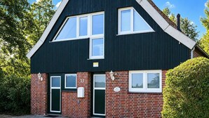 A two-story building with a dark facade, red brick lower section, and a green door. - The Zugvogel vacation home offers a cozy first floor apartment in a quiet, secluded location near the North Sea - ideal for families and dog owners looking to relax in the fenced garden and natural surroundings. (Wangerland)