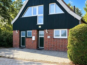 Ein zweistöckiges Gebäude mit dunkler Fassade, einem roten Backstein-Unterteil und einer grünen Tür.