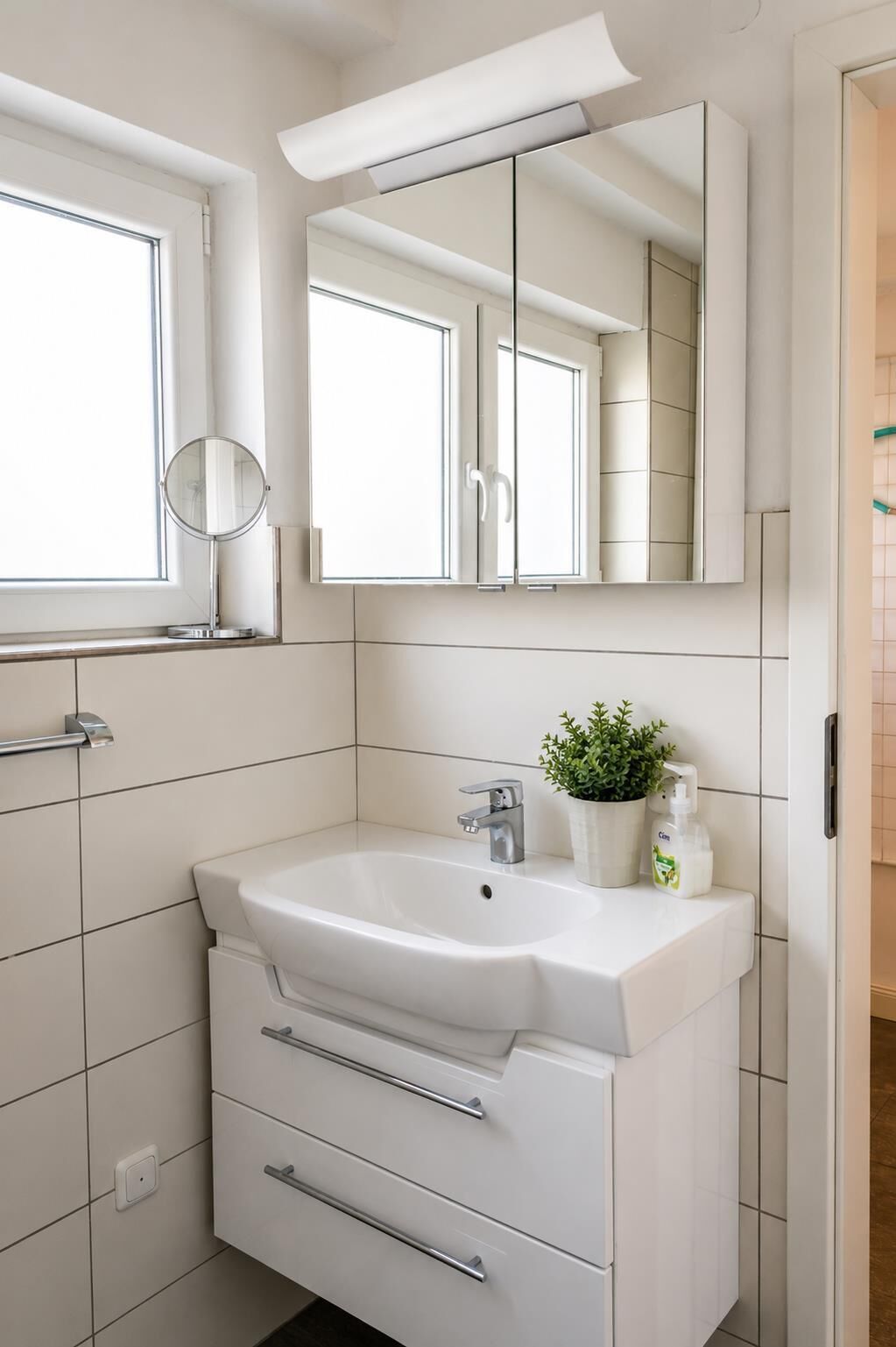 A bathroom with a white sink, a mirror, and a window.
