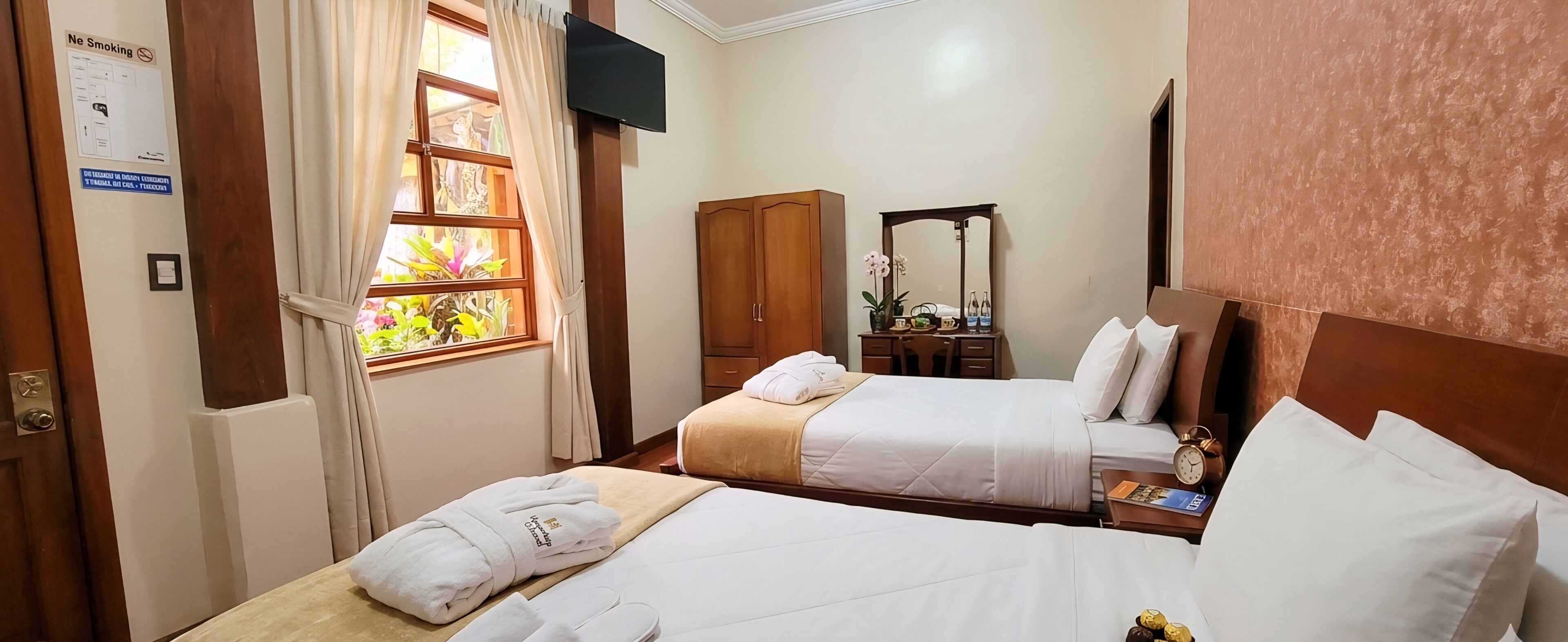 Habitación de hotel con dos camas, un armario de madera, un escritorio con espejo y una ventana con cortinas.