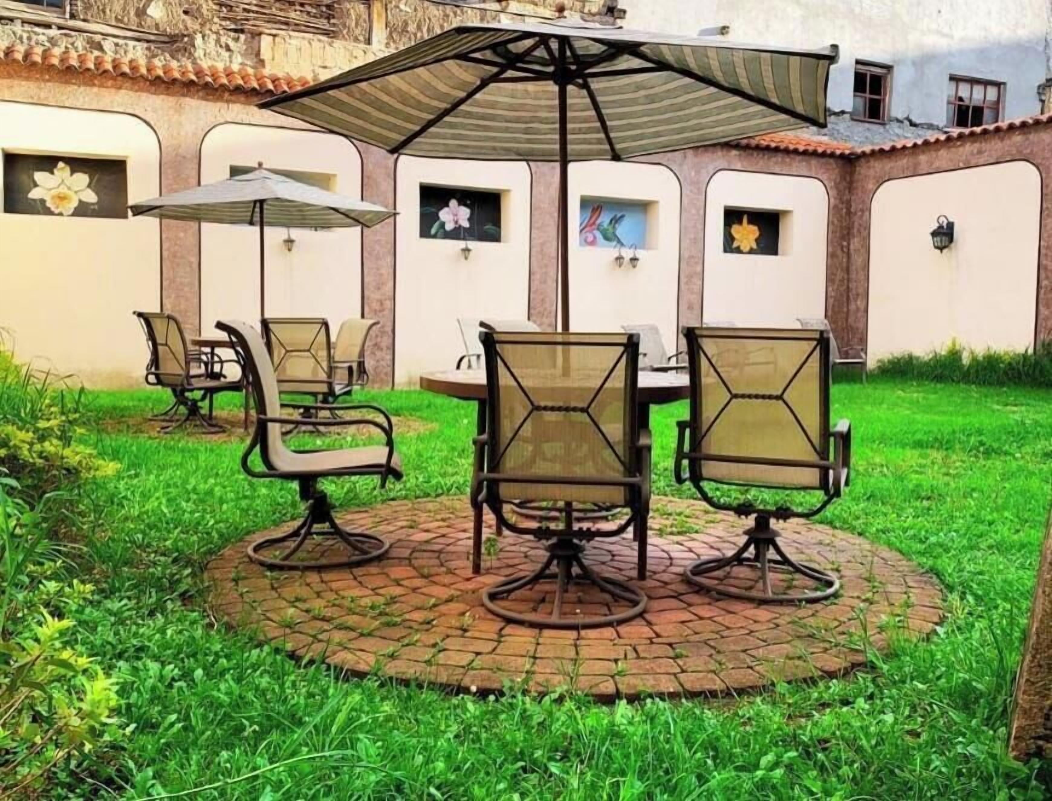 Un patio con una mesa redonda y sillas, rodeado por un borde de ladrillo.