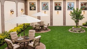 A patio with a dining table, chairs, and umbrellas, surrounded by a well-maintained lawn and decorative plants. - Hotel Pegasus (Cuenca)