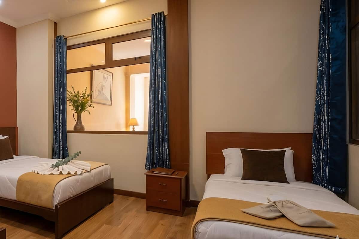 Une chambre dâhĂŽtel avec deux lits, une fenĂȘtre avec des rideaux, un tableau au mur et un plateau avec une tasse et des biscuits.
