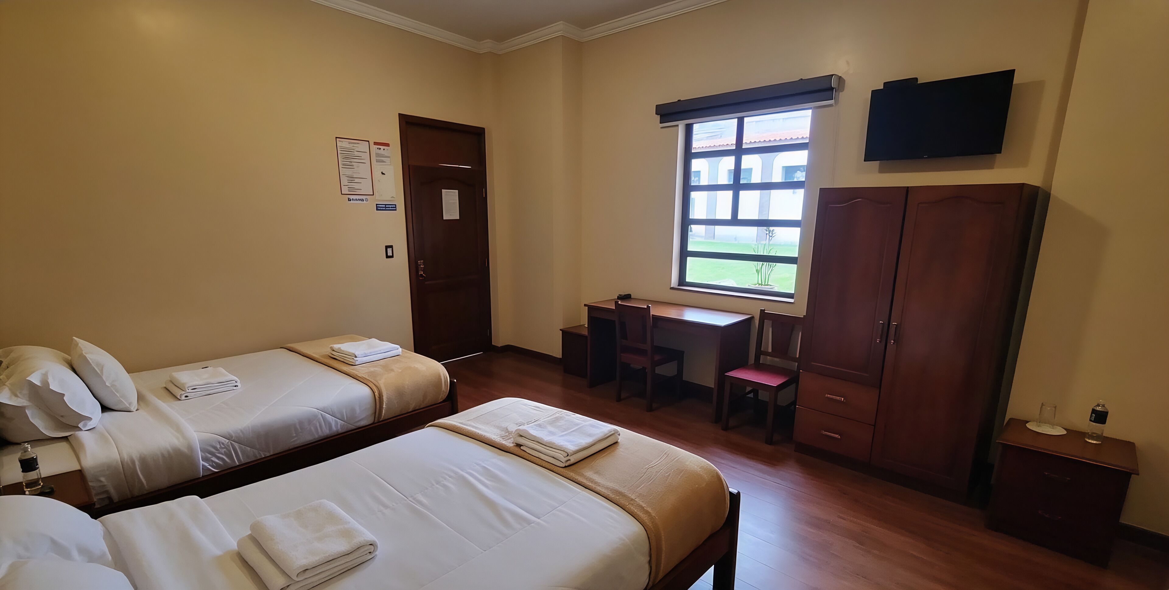 A hotel room with two beds, a desk, a chair, a wardrobe, and a television.