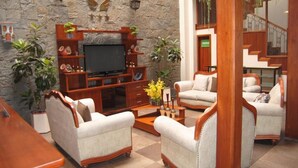 A living room with a stone wall, wooden entertainment unit, and two armchairs. - Hotel Pegasus (Cuenca)