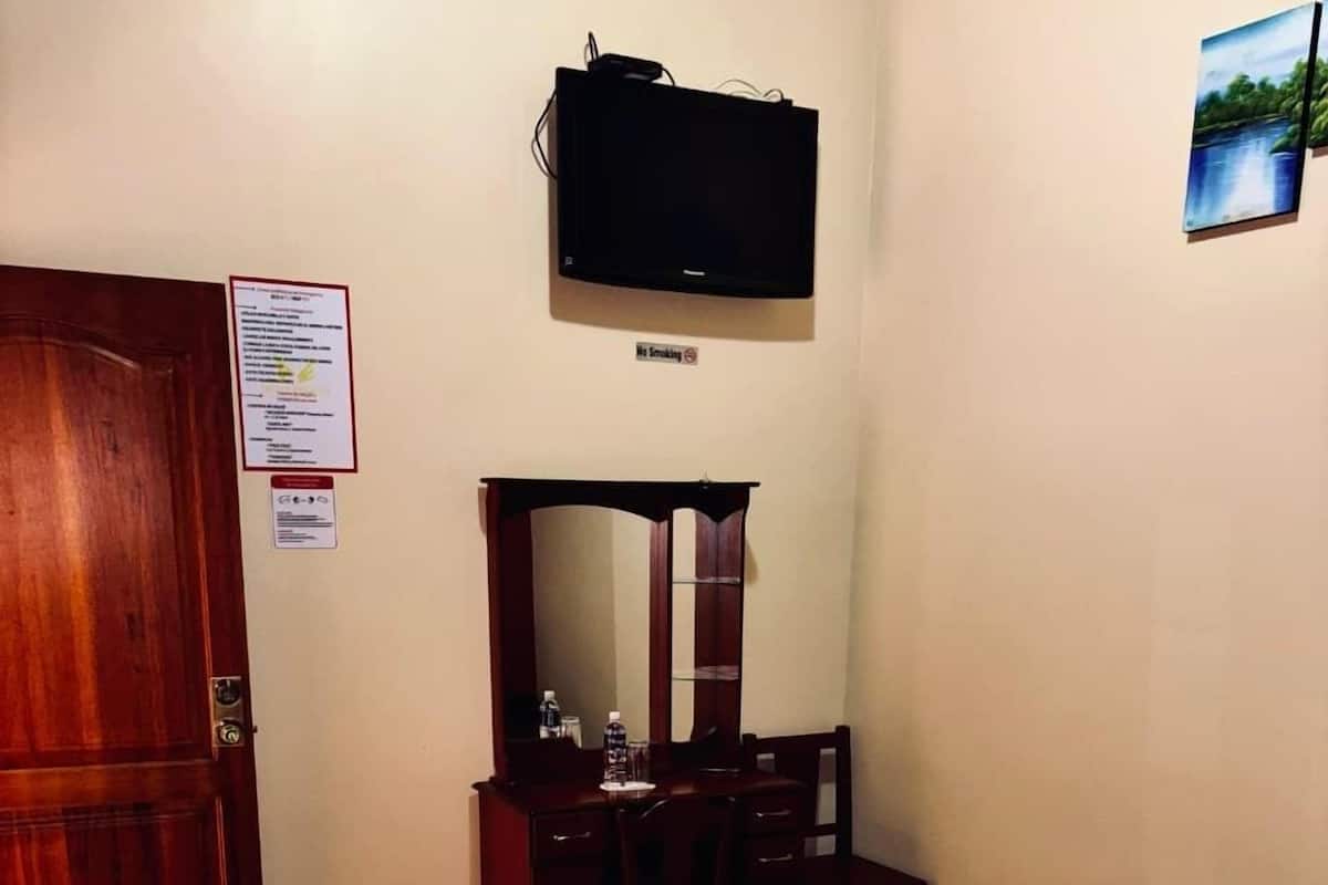 Una habitación de hotel con piso de madera, una cama con ropa blanca, un aparador de madera, un espejo y un televisor montado en la pared.