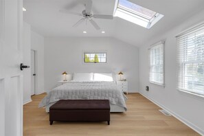 Ein Schlafzimmer mit einem Bett, zwei Nachttischen, einem Deckenventilator, einem Oberlicht und einem Fenster.