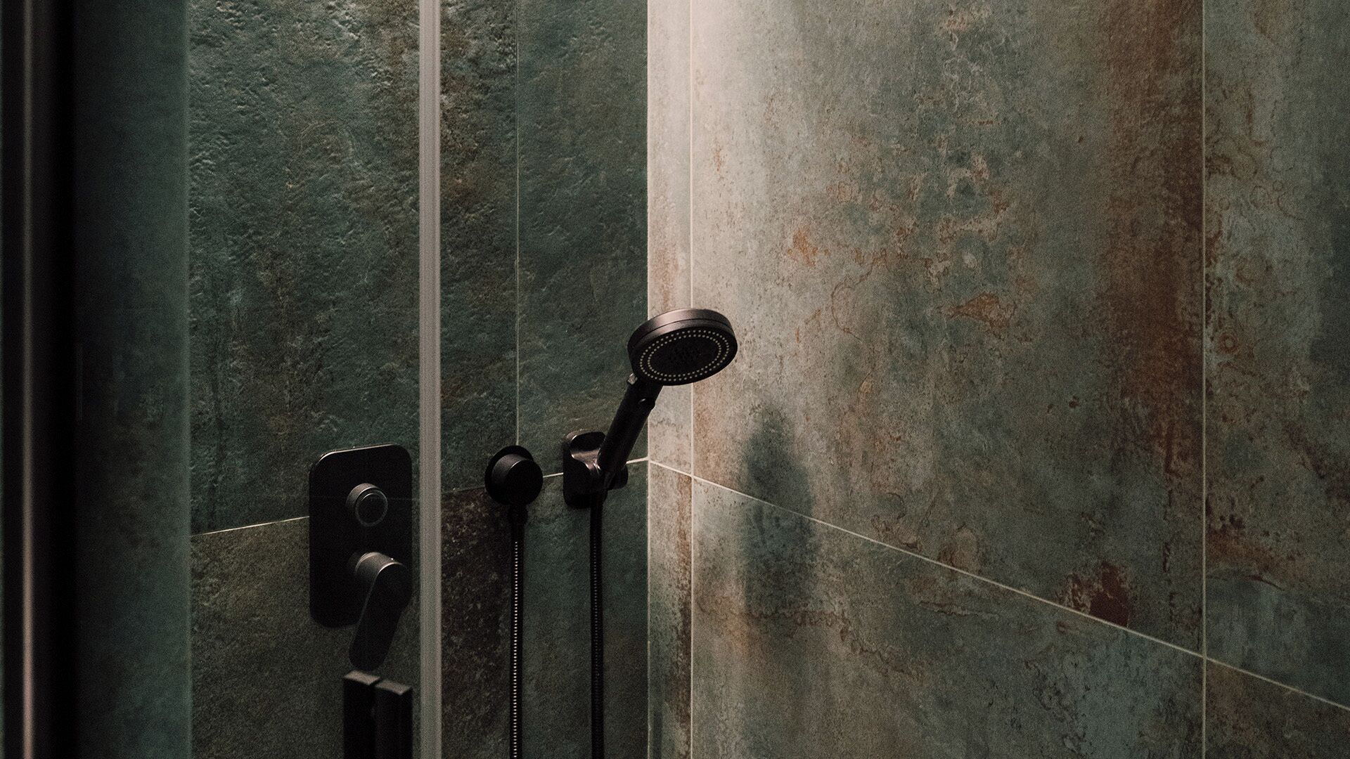 A shower with a handheld showerhead and a wall-mounted control panel.