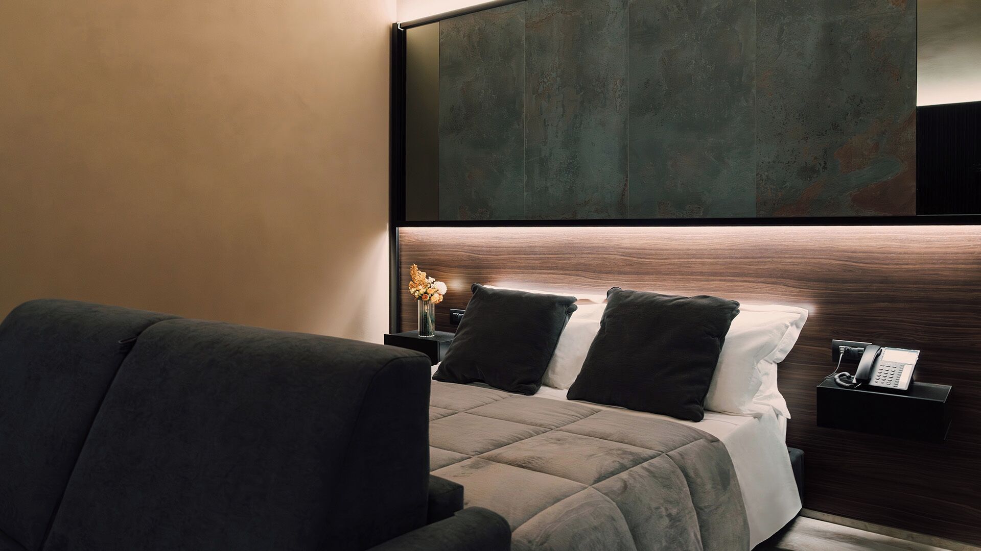 A modern hotel room with a bed, a chair, a nightstand, and a large abstract painting on the wall.
