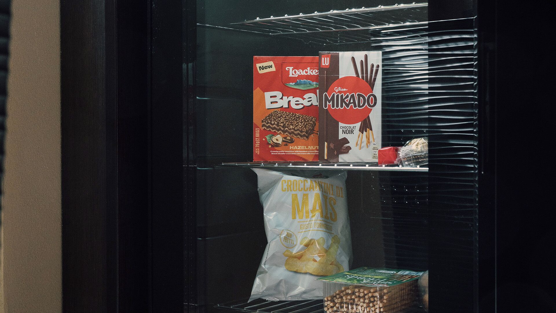 Ein Kühlregal mit verpackten Lebensmitteln, darunter eine Packung Toaster Bread, eine Tüte Croccantini und eine Schachtel mit Schokoladenkeksen.