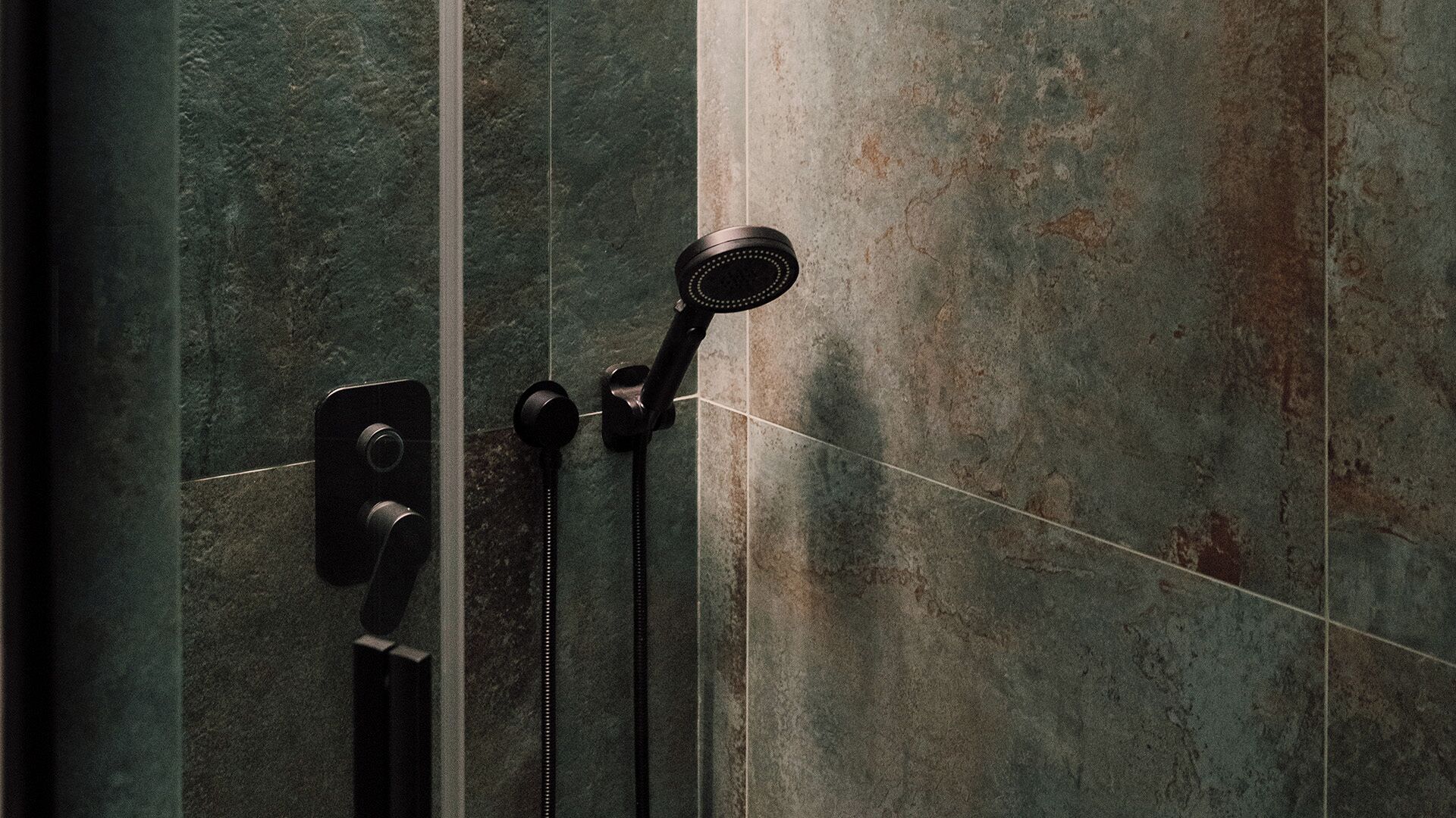 A shower with a handheld showerhead and a fixed wall-mounted showerhead, both mounted on a textured wall.
