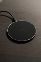 Un cargador inalámbrico circular, negro, sobre una superficie de madera.