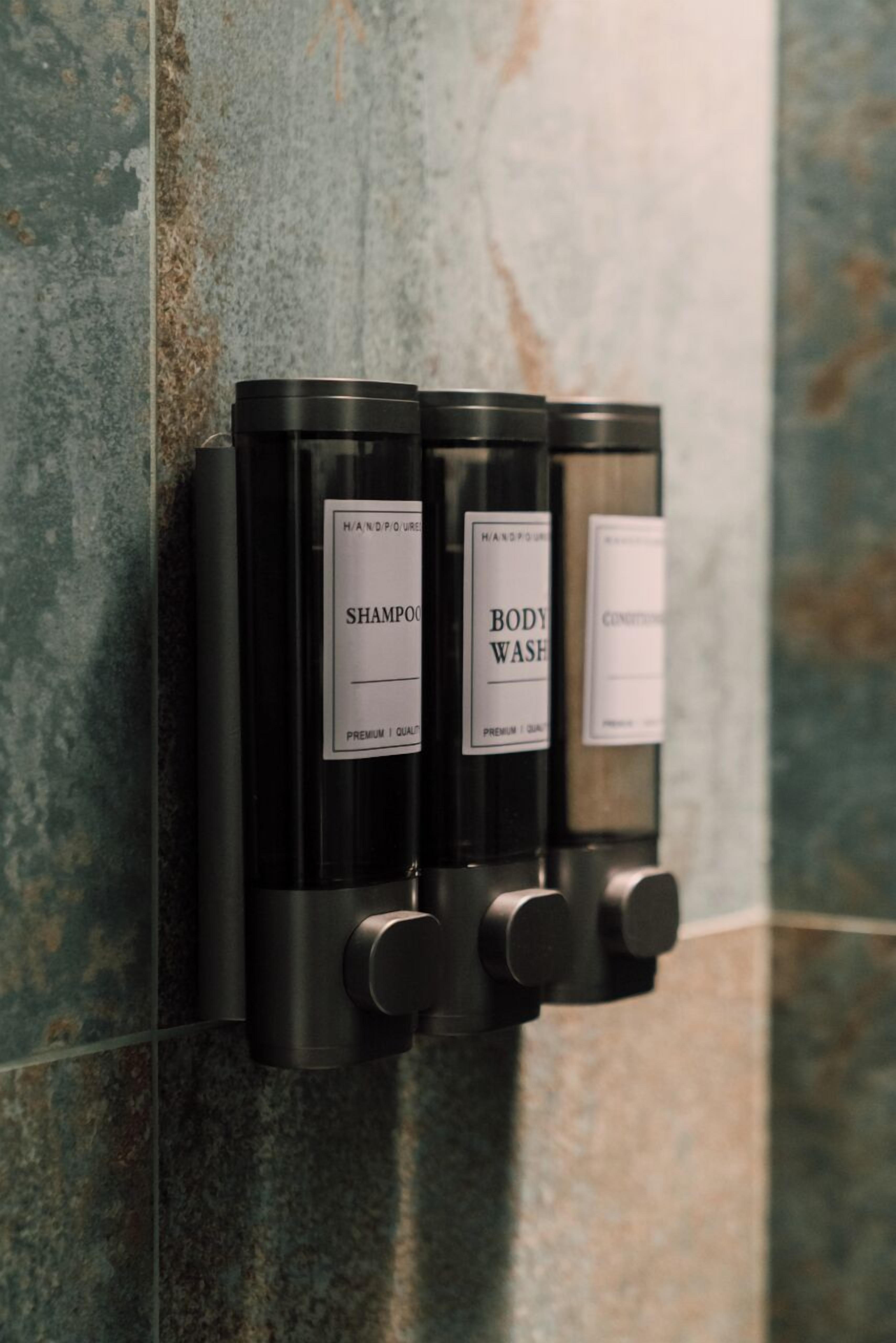 Un distributeur mural doté de deux flacons étiquetés « SHAMPOO » et « GEL DOUCHE ».