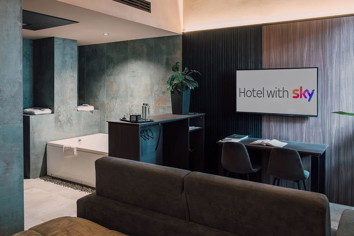 Quarto de hotel moderno com uma cama grande, uma escrivaninha, uma cadeira, uma banheira e uma planta.