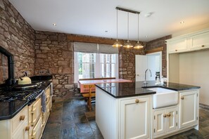 A kitchen with a stone wall, a stove, a sink, and a window with a view.