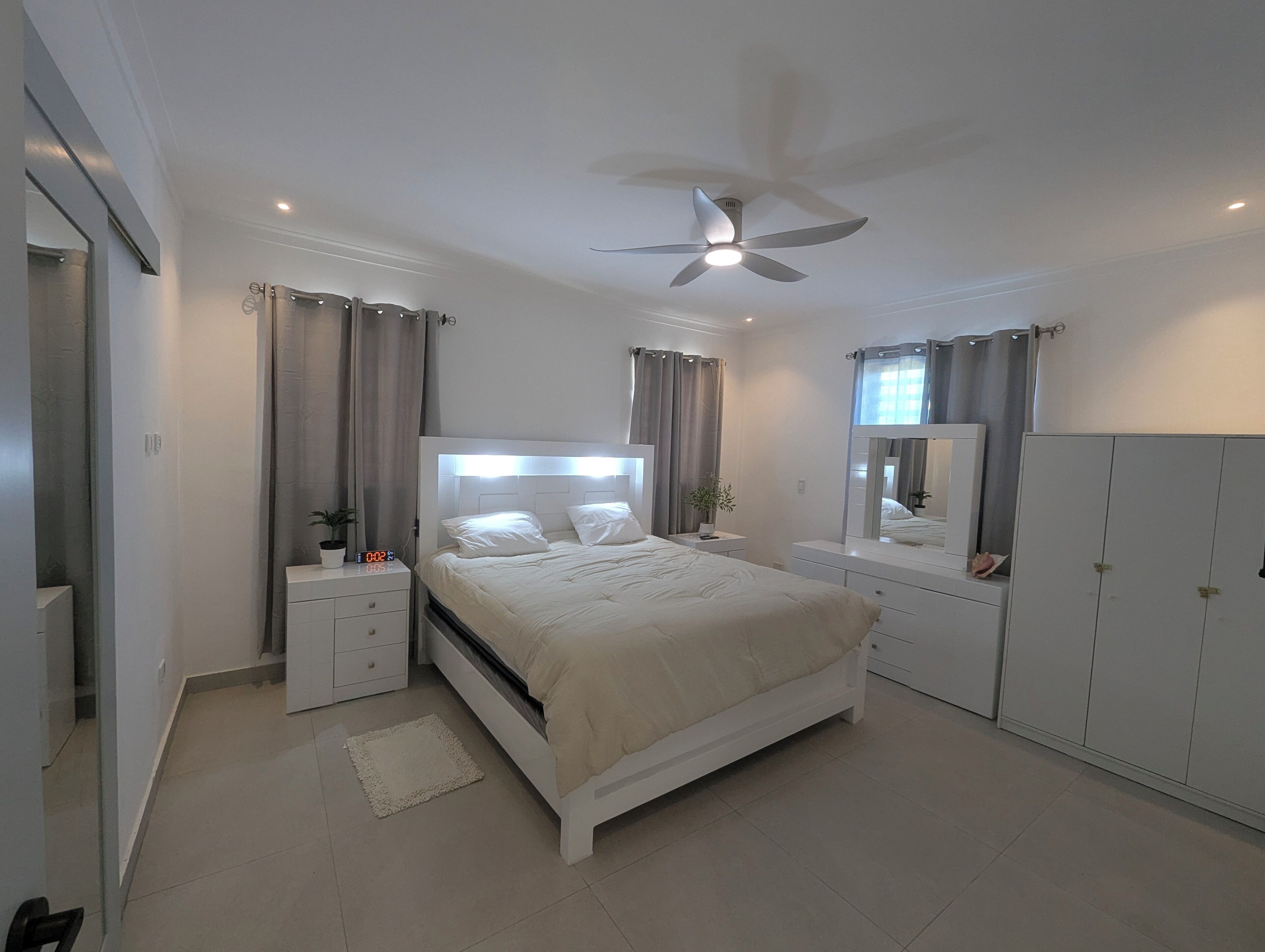 Ein Schlafzimmer mit einem Bett, Nachttischen, einem Deckenventilator, einem Spiegel und einem Kleiderschrank.