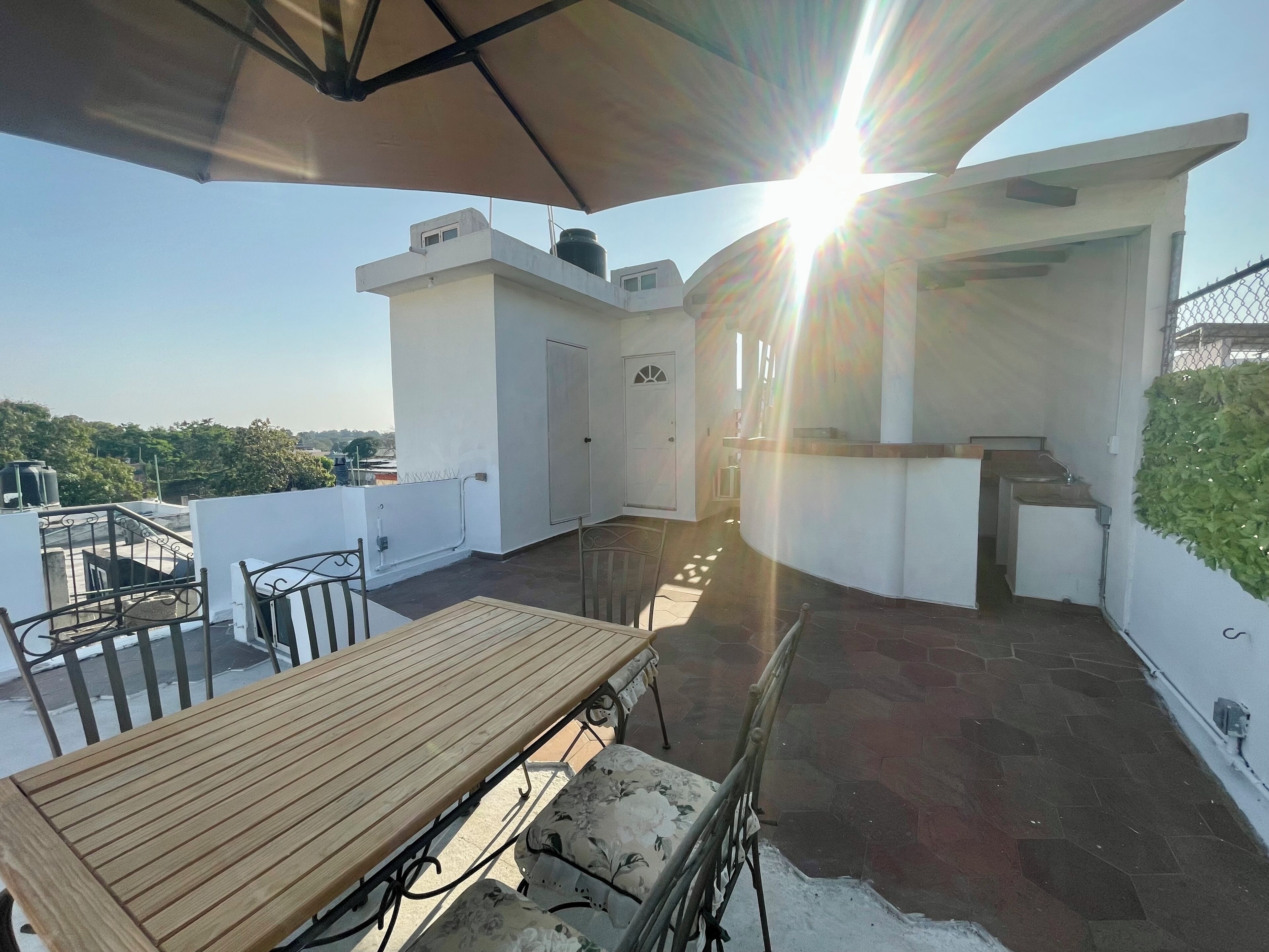 Una terraza en la azotea con mesa de madera, sillas, una pequeña barra y vistas a la ciudad.