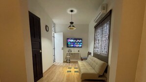 Un pasillo con piso de madera, un sofá, un televisor y un equipo de aire acondicionado.