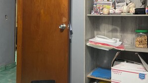 Una habitación con una puerta de madera, un estante con varios objetos, incluyendo un calendario, una pelota de béisbol y una caja con la etiqueta 'Priority Mail'.