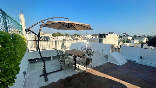 Una terraza en la azotea con una mesa, sillas, baranda metálica y vistas de la ciudad.
