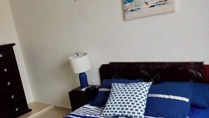 Una cama con ropa de cama a rayas, un cabecero oscuro, una mesita de noche con una lámpara y un cuadro en la pared.