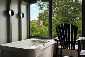 Ein Badezimmer mit einer Badewanne, einem Sessel und einem Fenster mit Blick auf Bäume.