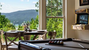 Une table de billard avec une vue panoramique, une table à manger avec des verres et une carafe, et un téléviseur posé sur une étagère.