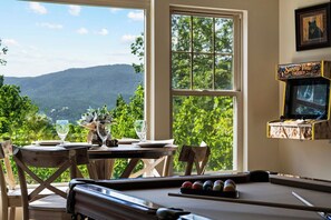 Ein Billardtisch mit schöner Aussicht, ein Esstisch mit Gläsern und einer Kanne sowie ein Fernseher auf einem Regal.
