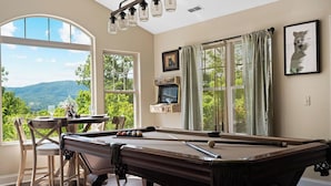 Une table de billard avec vue sur les montagnes, une table avec des chaises et un téléviseur d’époque.