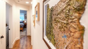 Un pasillo con obras de arte enmarcadas en la pared, una puerta que da a un dormitorio y suelo de madera.