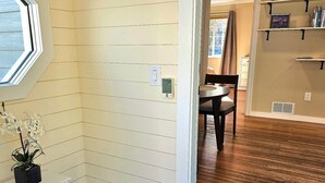 A room with a wooden floor, a white wall with horizontal lines, a white bench, a door with a doormat, and a window with a view. - Downtown home w/patio in historic Pilot's Row (Anchorage)