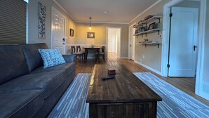 A living room with a sofa, coffee table, and a dining area with chairs and a table. - Downtown home w/patio in historic Pilot's Row (Anchorage)