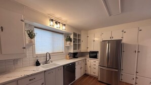 A modern kitchen with white cabinets, a stainless steel refrigerator, a microwave, and a sink. - Downtown home w/patio in historic Pilot's Row (Anchorage)