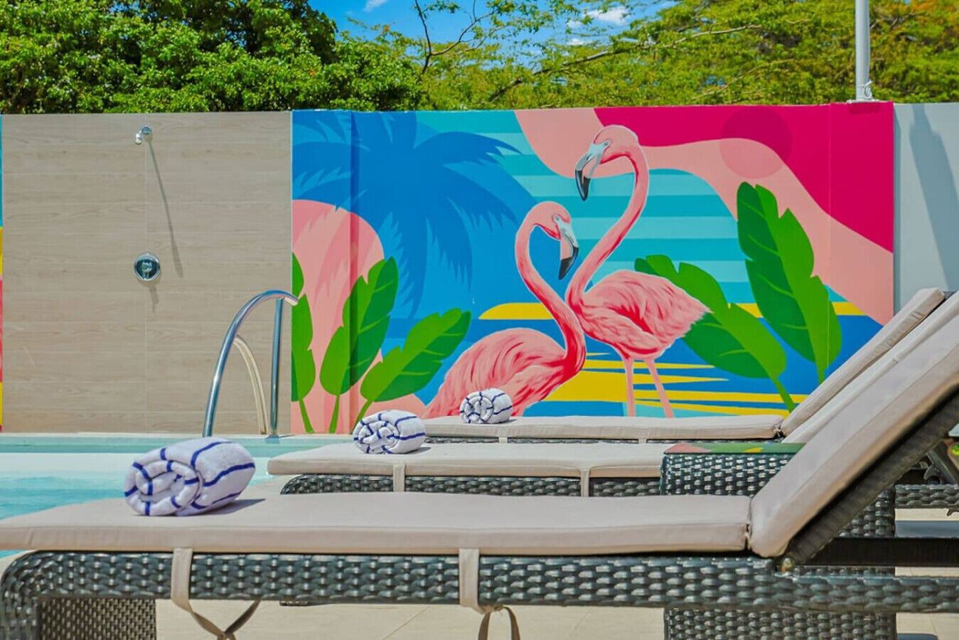 A poolside area with lounge chairs, a towel, and a decorative wall with flamingos and palm leaves.