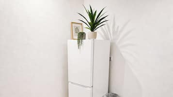 Un refrigerador blanco con una planta encima, un basurero y un cuadro en la pared.