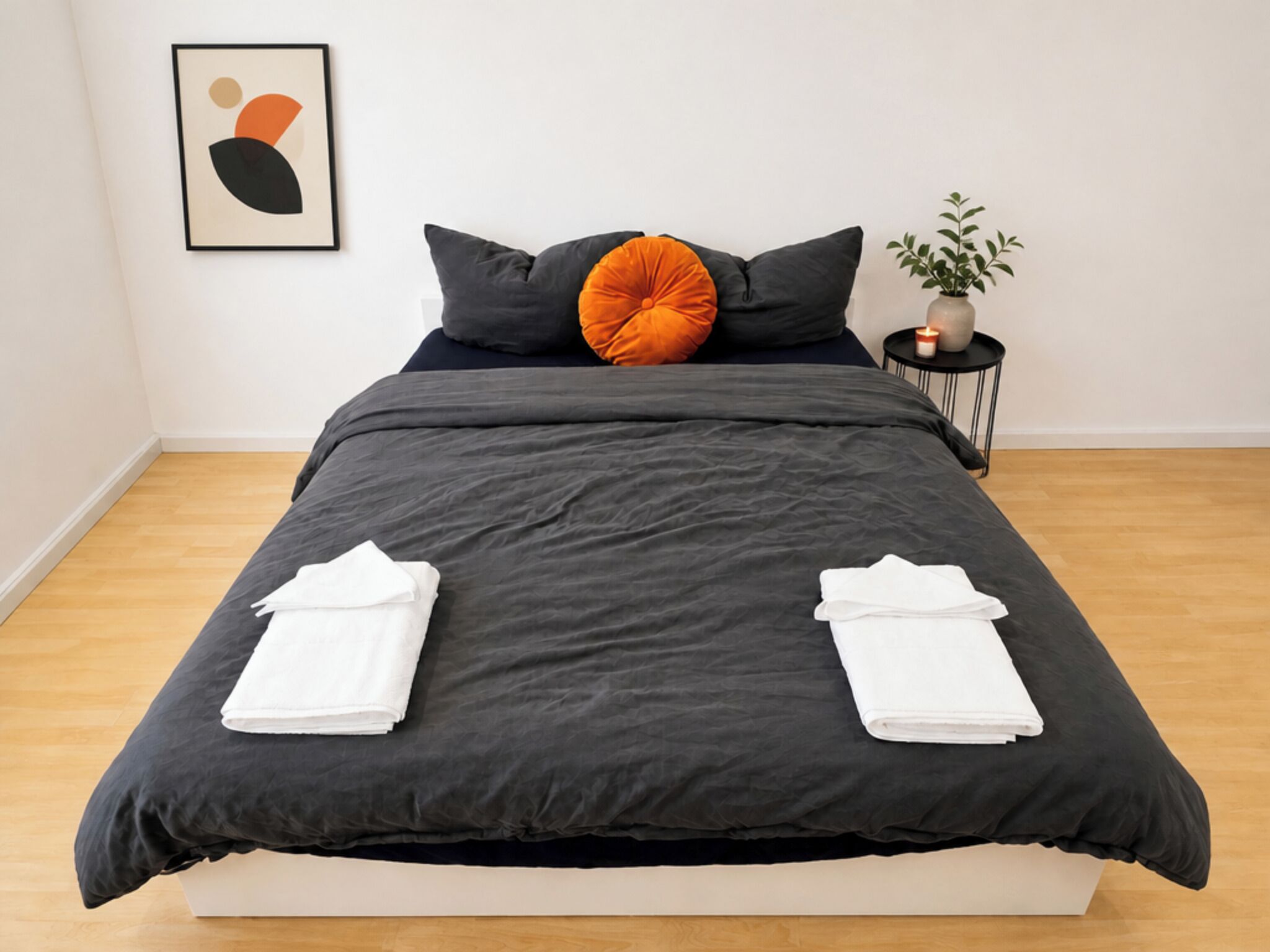 Un lit recouvert d’une couvre-lit gris foncé, deux serviettes blanches et un seul oreiller orange.