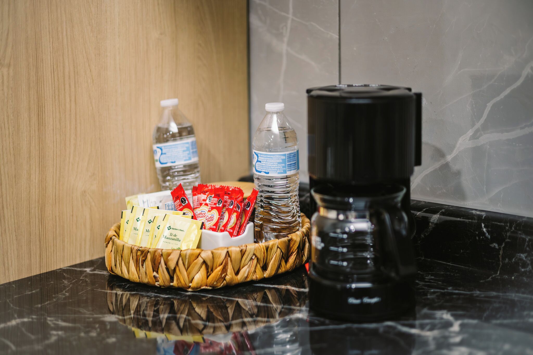 Une machine à café, des bouteilles d’eau et un panier contenant des sachets de café, le tout posé sur un comptoir en marbre.