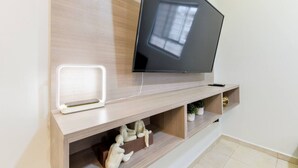 Ein modernes Wohnzimmer mit einem Flachbildfernseher an einer Holzwand, einer weißen Unterhaltungsanlage darunter und einem kleinen Regal mit Dekorationen.