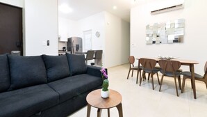 Ein modernes Wohnzimmer mit einer Couch, einem Esstisch mit Stühlen, einem kleinen runden Tisch mit Pflanze und einer Küchenzeile im Hintergrund.