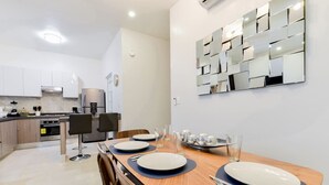 Eine moderne Küche mit weißen Schränken, einem Edelstahlkühlschrank und einem Essbereich mit einem Holztisch, gedeckt für zwei Personen.