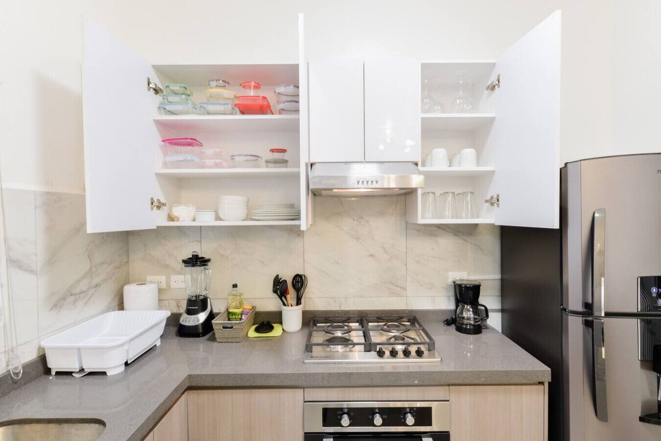 Una cocina moderna con armarios blancos, estufa a gas, refrigerador y horno empotrado.