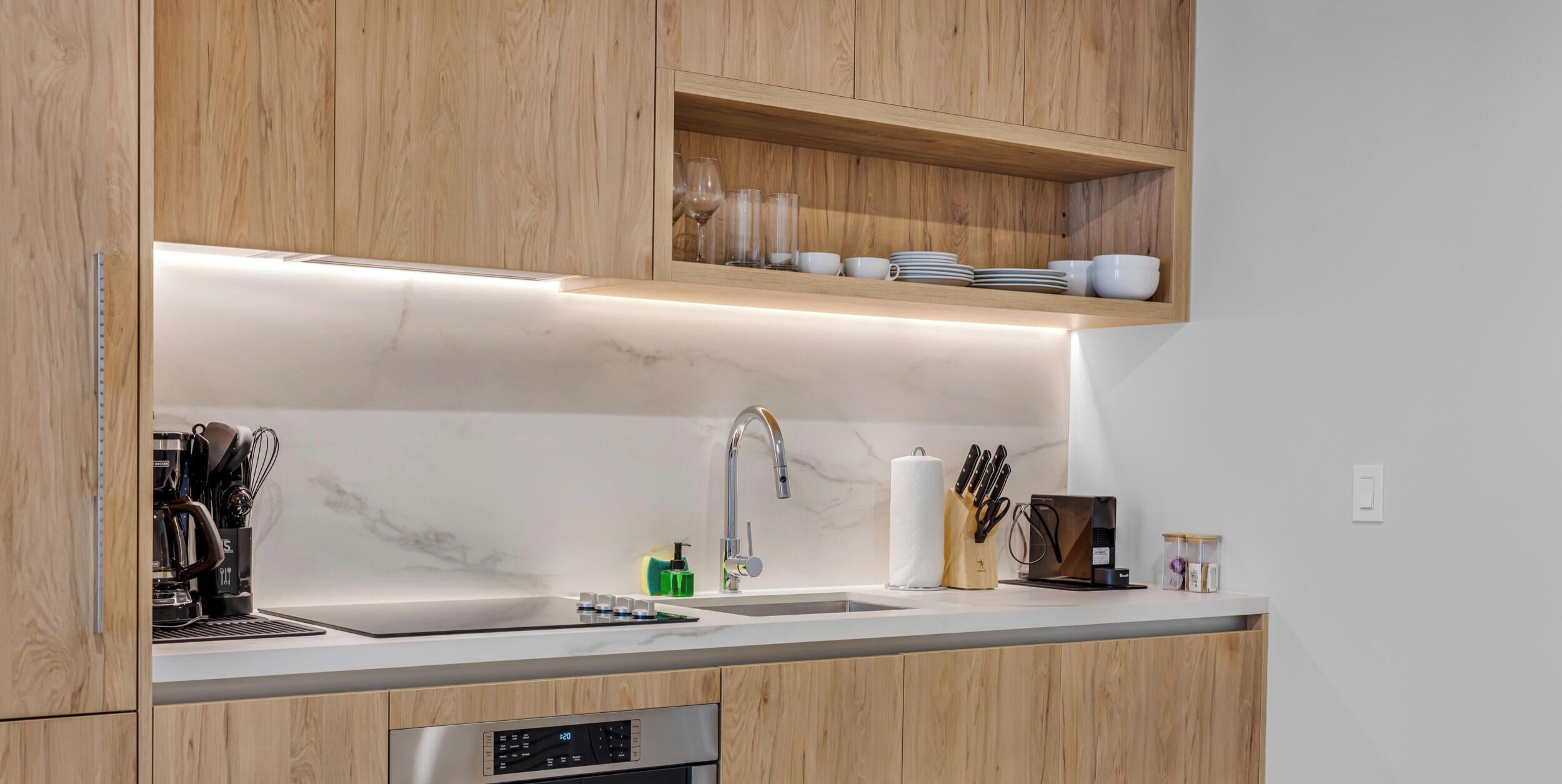 A modern kitchen with wooden cabinets, a marble countertop, a built-in sink, and a coffee machine.