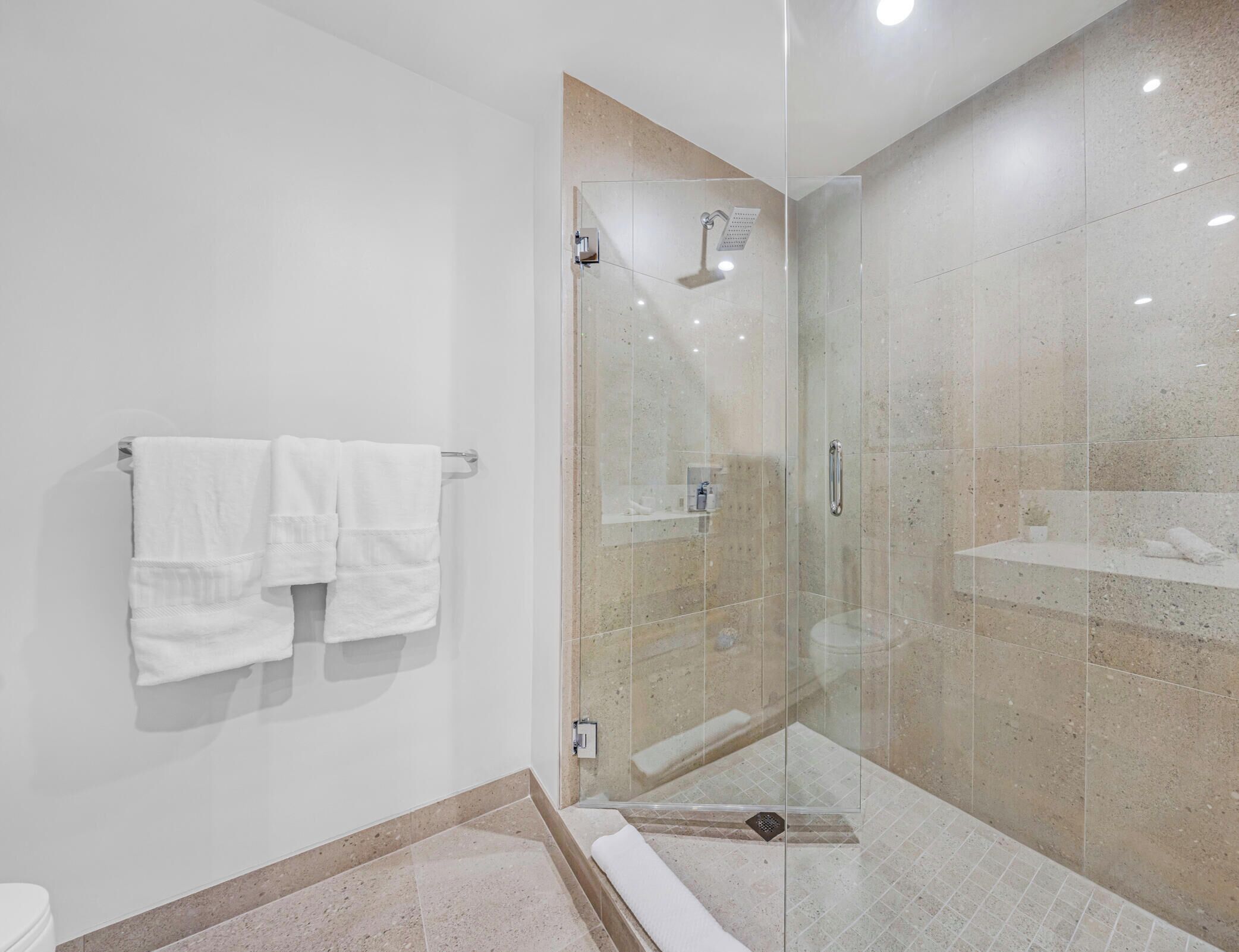 Ein modernes Badezimmer mit einer Duschkabine, einer weißen Toilette und einem Handtuchhalter mit zwei Handtüchern.