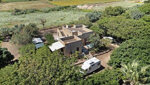 A modern house with a patio, surrounded by dense greenery and a parked camper. - Villa 'Diego' with Sea View, Wi-Fi and Air Conditioning (Favignana)
