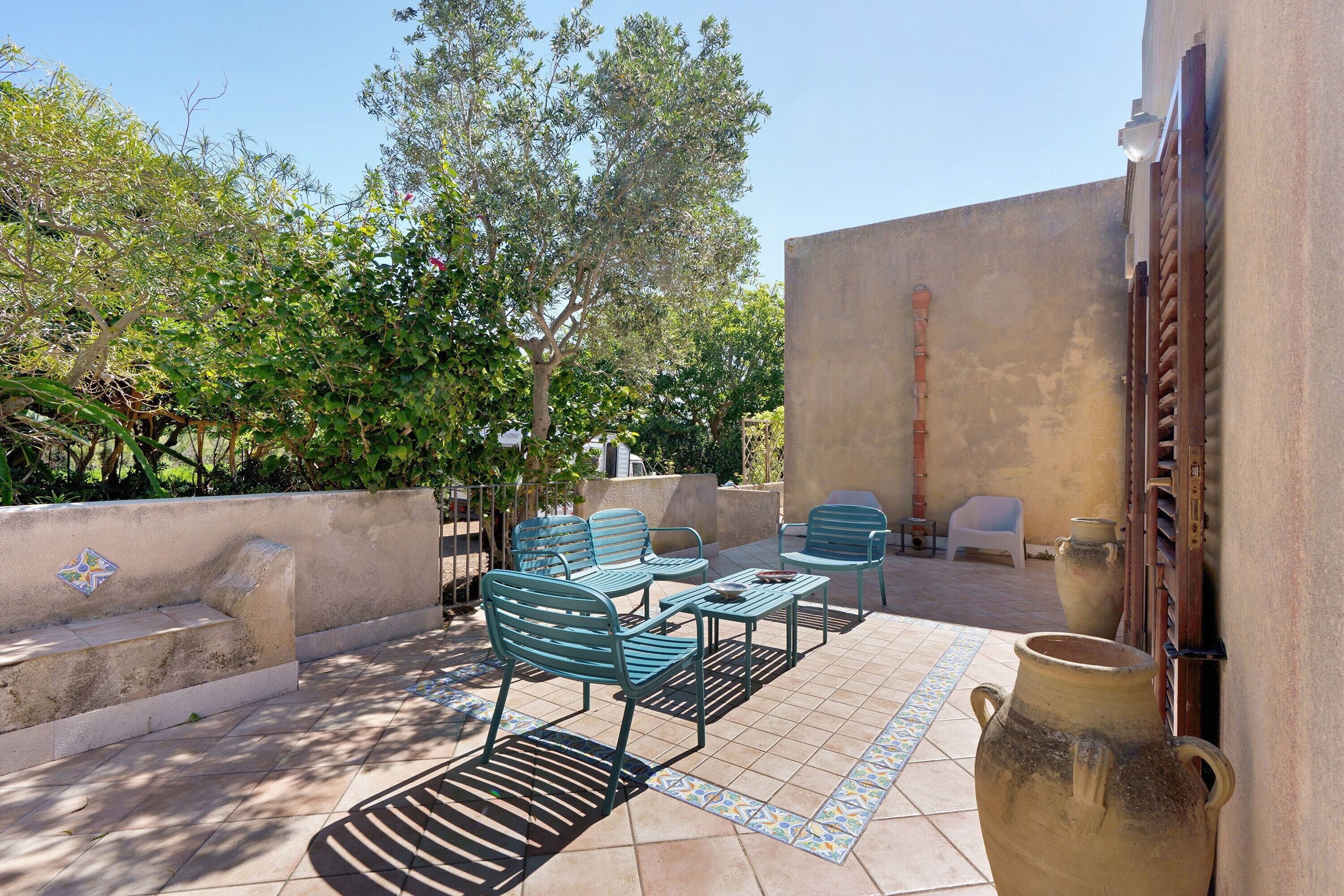 An outdoor patio with metal chairs and tables, a large ceramic pot, and a white plastic chair.