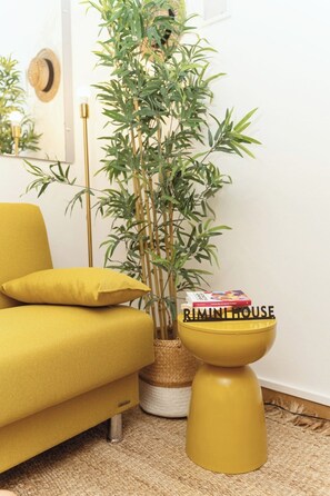 Ein gelbes Sofa, eine Bambuspflanze und ein kleiner Tisch mit einem Buch mit dem Titel 'RIMINI HOUSE'.