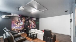 Ein Heimkino mit einer großen Wandmalerei, Ledersitzgelegenheiten, einem weißen Sofa und einem Projektor.