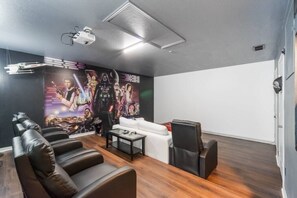 A home theater room with a large wall mural, leather seating, a white couch, and a projector. - 5-Bed Villa w/ Private Pool (Davenport)