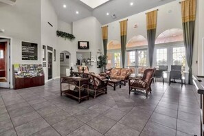 Eine geräumige Lobby mit einer Rezeption, einer Sitzecke mit Korbmöbeln und großen Fenstern mit Vorhängen.